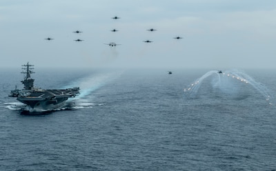 200602-N-VW723-1416 PACIFIC OCEAN (June 2, 2020) Aircraft from Nimitz Carrier Strike Group fly in formation over the aircraft carrier USS Nimitz (CVN 68) while an MH-60S Sea Hawk helicopter, from the "Battle Cats" of Helicopter Maritime Strike Squadron (HSM) 73. Nimitz is underway conducting composite training unit exercise (COMPTUEX). COMPTUEX is an intensive exercise designed to fully integrate units of the carrier strike group, while testing a strike group's ability as a whole to carry out sustained combat operations from the sea. (U.S. Navy photo by Mass Communication Specialist 3rd Class Keenan Daniels/Released)