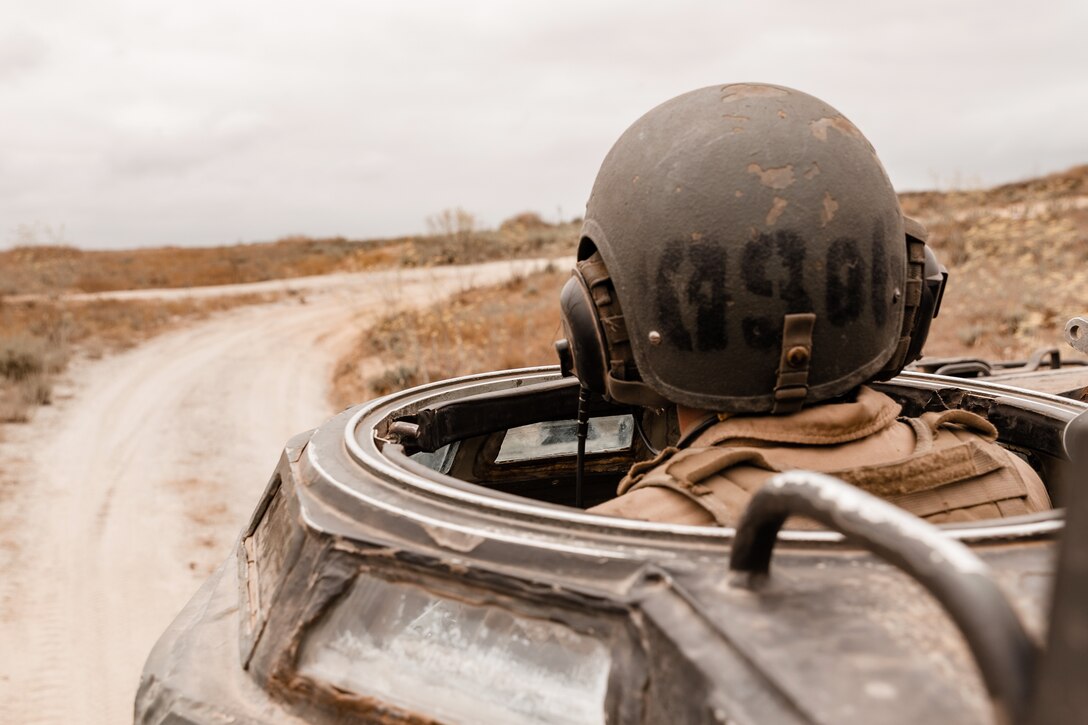 A Marine's head is seen from  a vehicle on a dirt road.