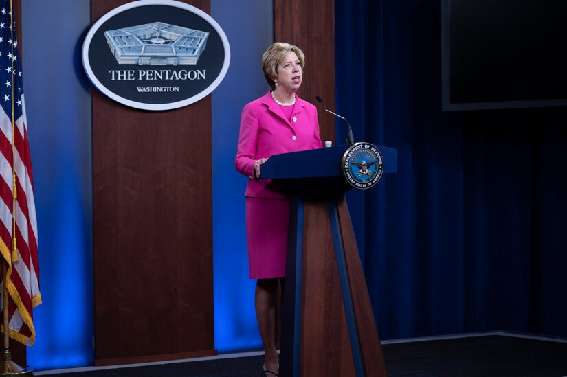 A woman stands at a lectern and speaks into a microphone.