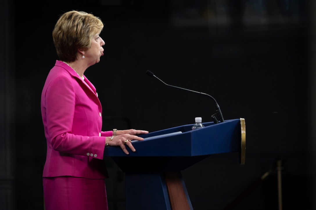 A woman stands at a lectern and speaks into a microphone.