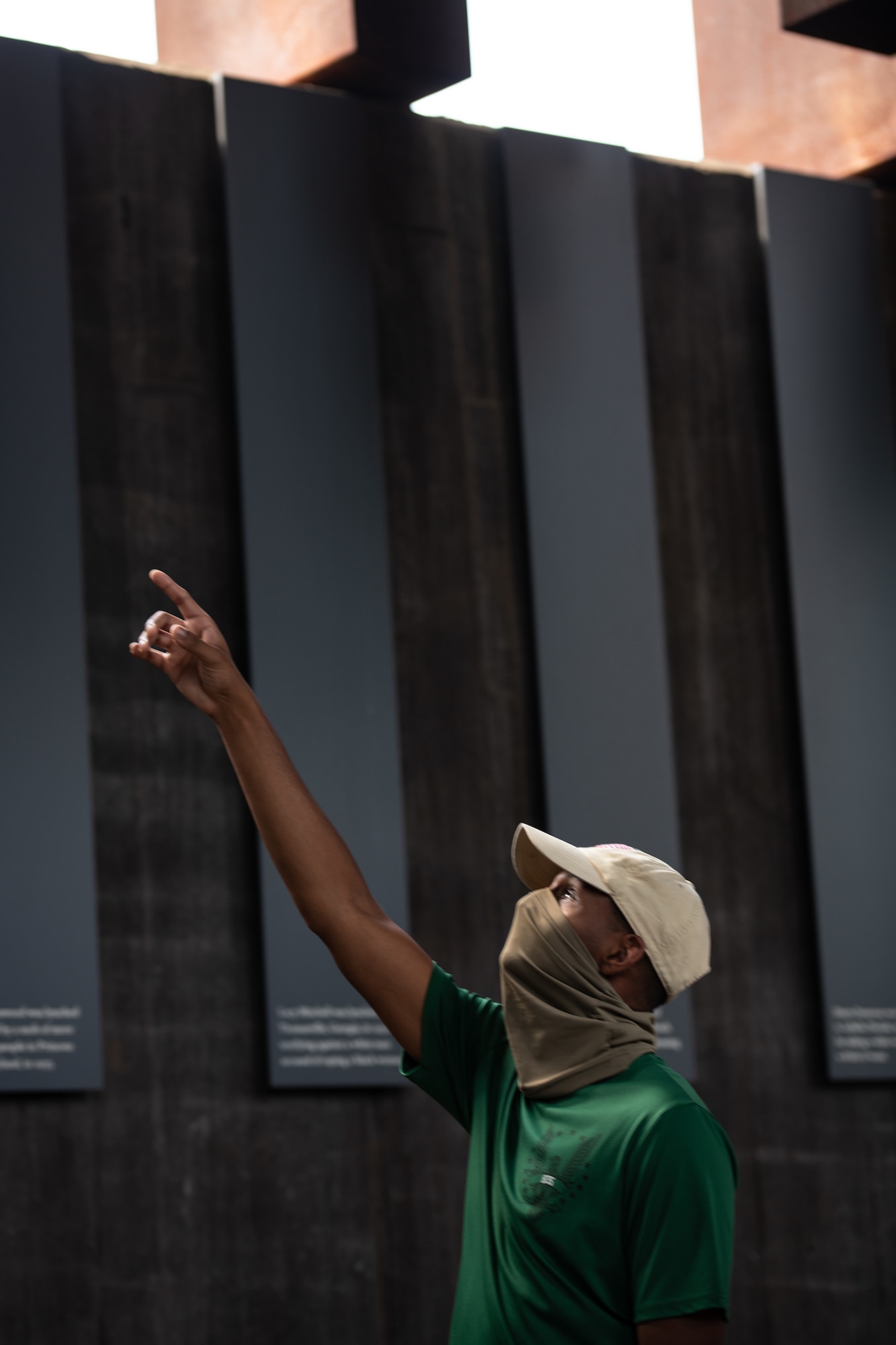 An Air Force Reserve Officer Training Corps cadet training assistant looks up and points at one of the suspended monuments at The National Memorial for Peace and Justice.