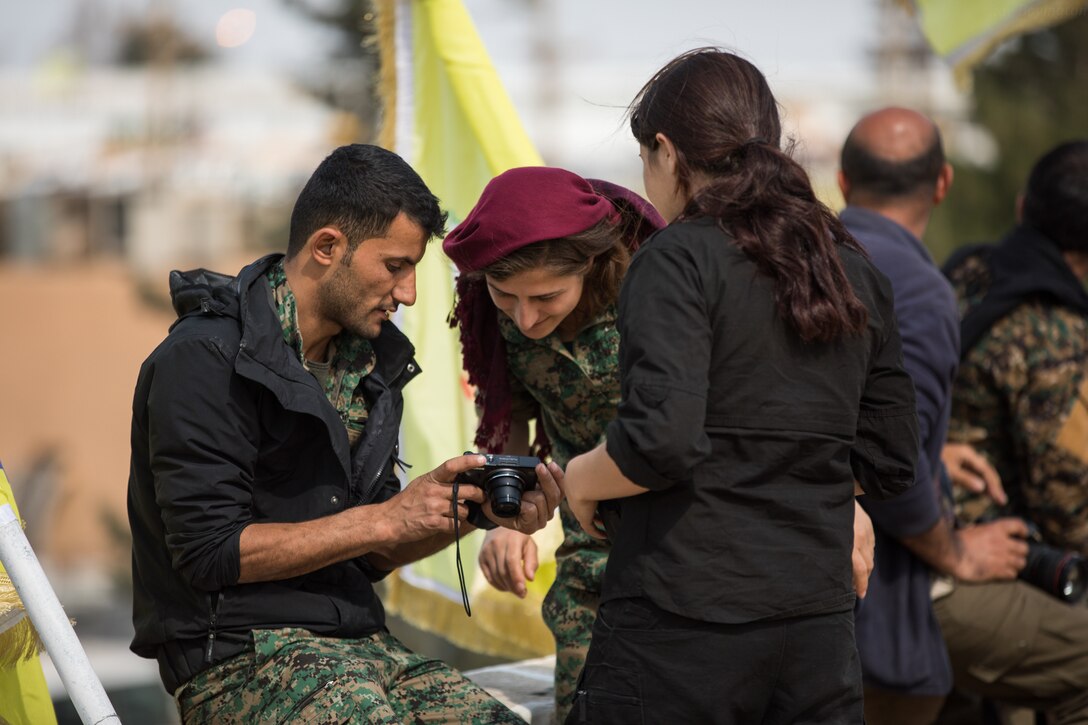 A Syrian Democratic Forces member shows fellow members photos he captured during a victory announcement ceremony over the defeat of Daesh’s so-called physical caliphate Mar. 23, 2019 at Omar Academy, Deir ez-Zor, Syria. The Global Coalition will continue addressing the threat Daesh continues to pose to the partner nations and allies, while preventing any return or resurgence in liberated areas. (U.S. Army photo by Staff Sgt. Ray Boyington)