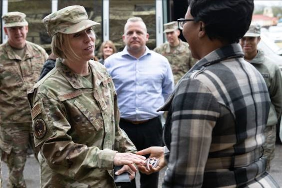 woman in uniform handing a coin to woman in civilian clothes with people watching