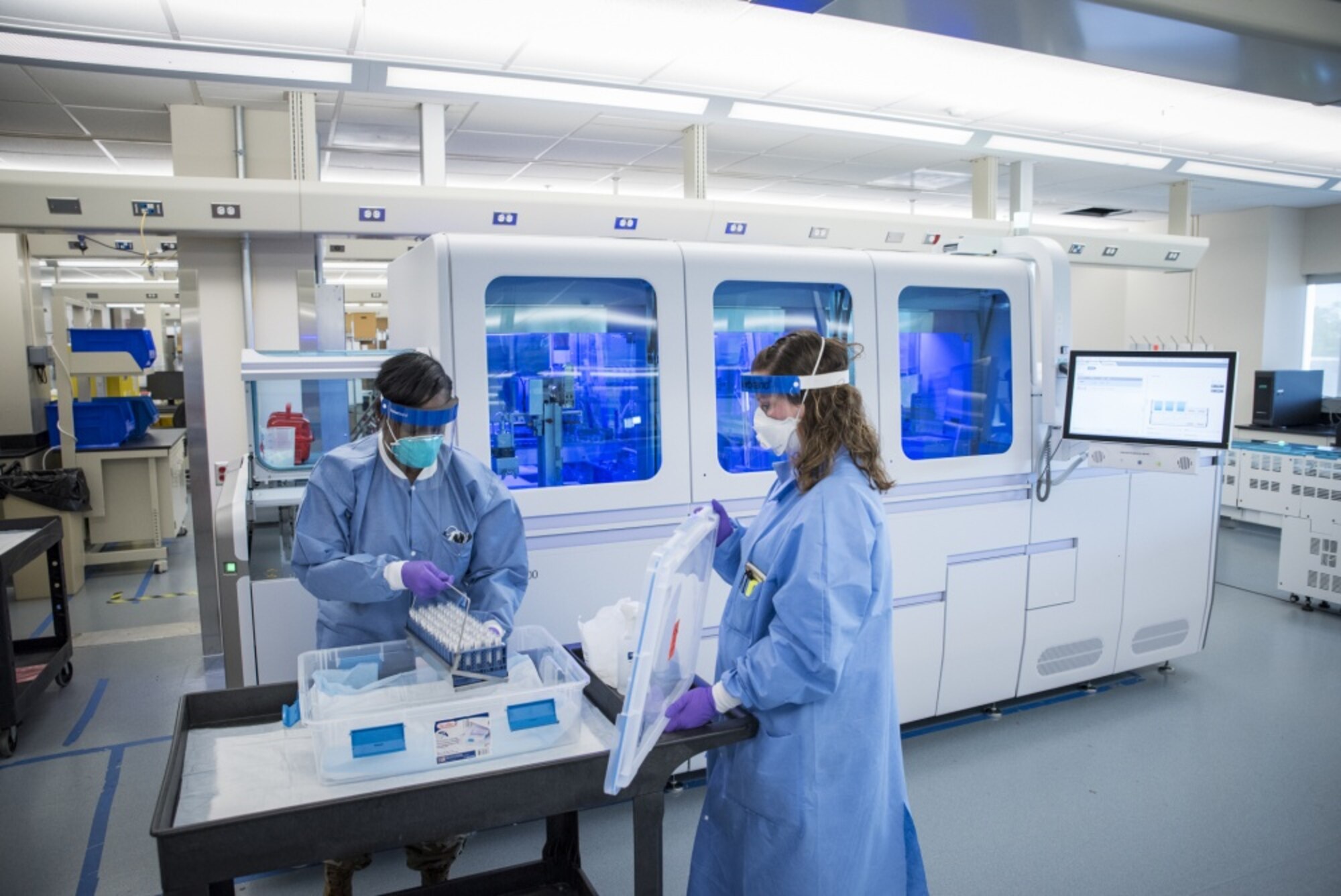 Image of Staff Sgt. Alexis Shodeke (left) and Renee Mayhon, medical laboratory technicians in the United States Air Force School of Aerospace Medicine’s Epidemiology Laboratory, preparing to load new samples onto the Roche 8800 for COVID polymerise chain reaction testing.