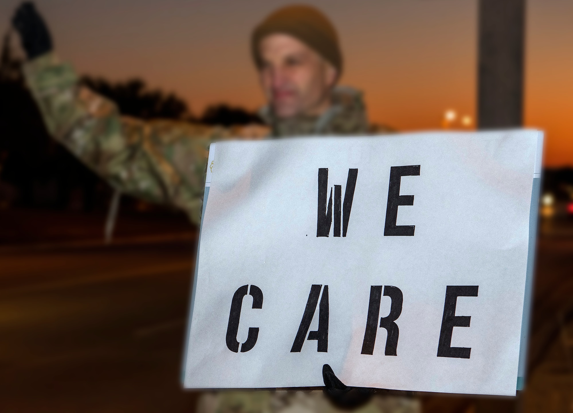 Lt. Col. Scott Christensen, 331st Training Squadron commander, holds a positive message of support at a base gate during the morning inbound commute as part of their new initiative, “We Care,” at Joint Base San Antonio-Lackland, Texas.