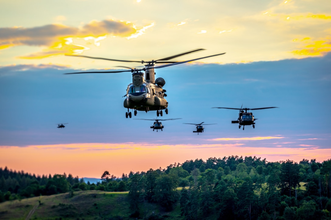 Five helicopters fly against a sky of pink, yellow and blue colors.