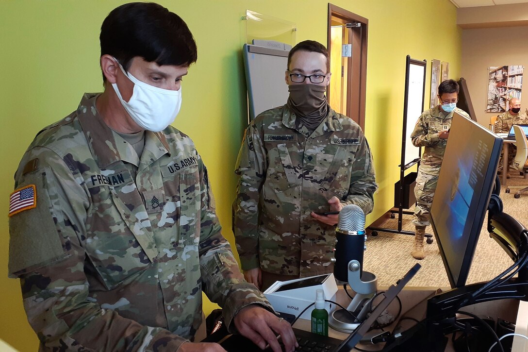 A soldier wearing a face mask configures a smartphone for another masked soldier.