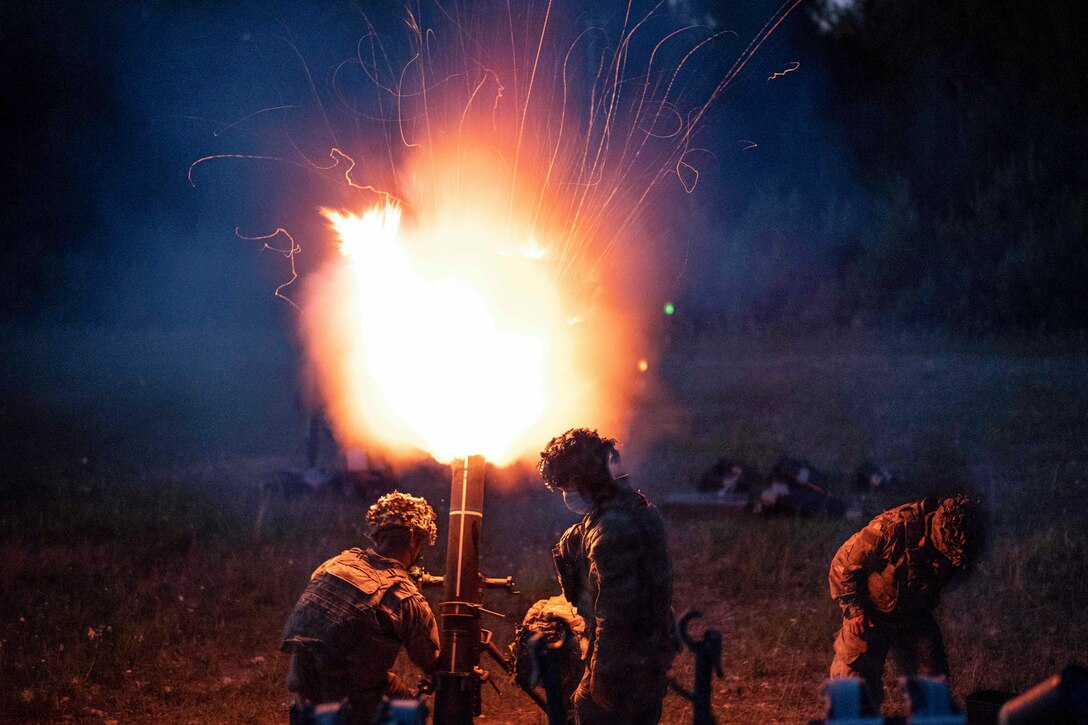 Soldiers fire an illumination round from a mortar system, lighting up a dark sky.