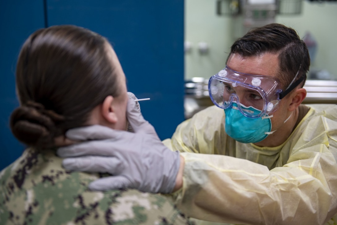 A female sailor is tested for COVID-19 by a health care provider wearing personal protective equipment.