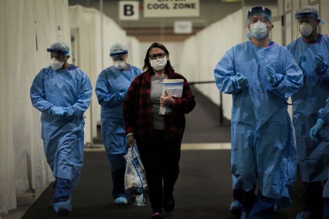 Flanked by four medical providers wearing personal protective gear, a woman leaves a field hospital.