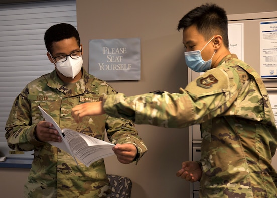 Two airmen wearing masks while holding paper