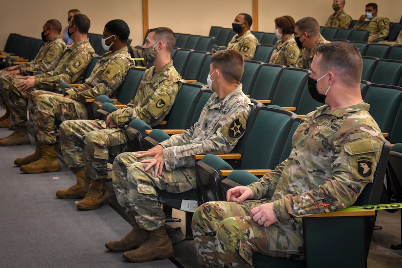 Soldiers sitting in a row wearing masks and social distanced.