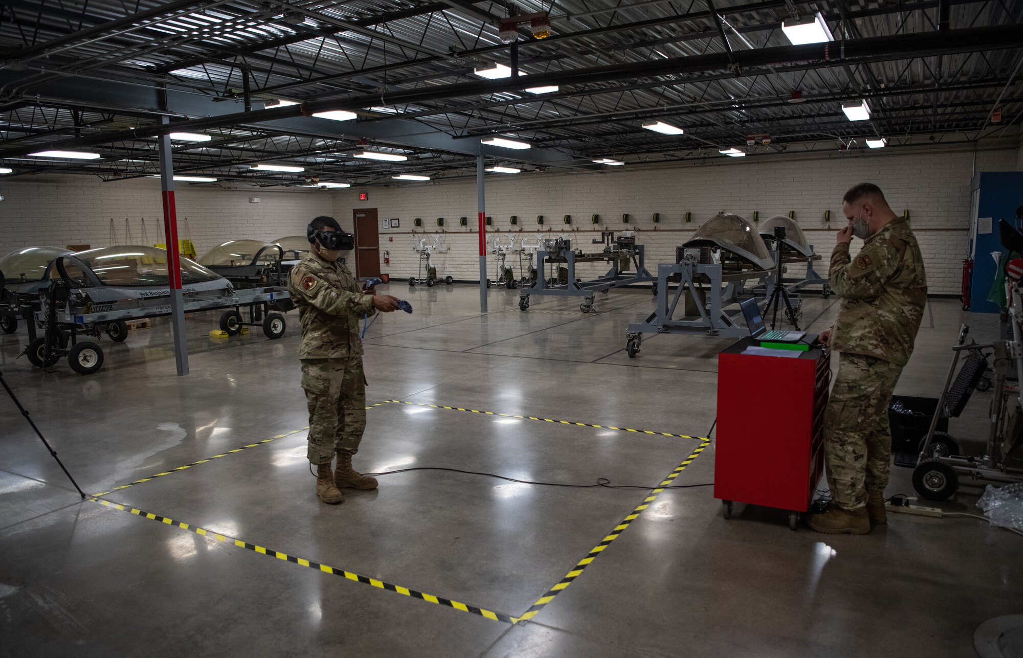 Airman 1st Class Delwyn Travillion, 56th Component Maintenance Squadron aircrew egress systems apprentice (left), trains on a virtual reality maintenance trainer while Tech. Sgt. Ian Rider, 56th CMS aircrew egress systems craftsman, monitors training July 13, 2020, at Luke Air Force Base, Ariz. The egress shop is responsible for the overall integrity of the emergency ejection seat system in the F-35A Lightning II. The egress shop implemented the virtual reality maintenance trainer to enhance training efficiency and reduce training time. (U.S. Air Force photo by Airman 1st Class Dominic Tyler)