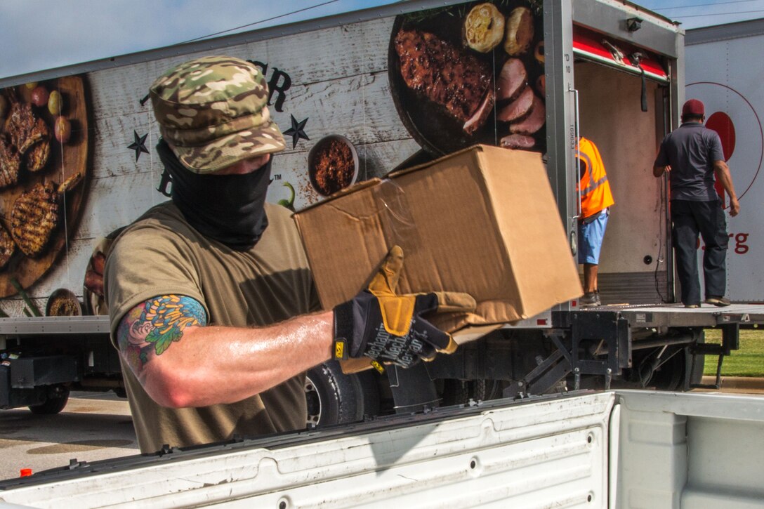 A guardsman wearing personal protective equipment carries a box of food during a food distribution event.
