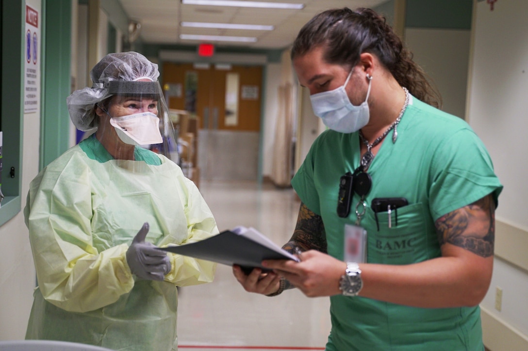 A medical volunteer wearing personal protective equipment reviews a checklist with a soldier.
