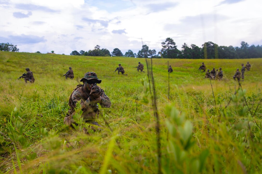A group of Marines take security positions in a grassy field.