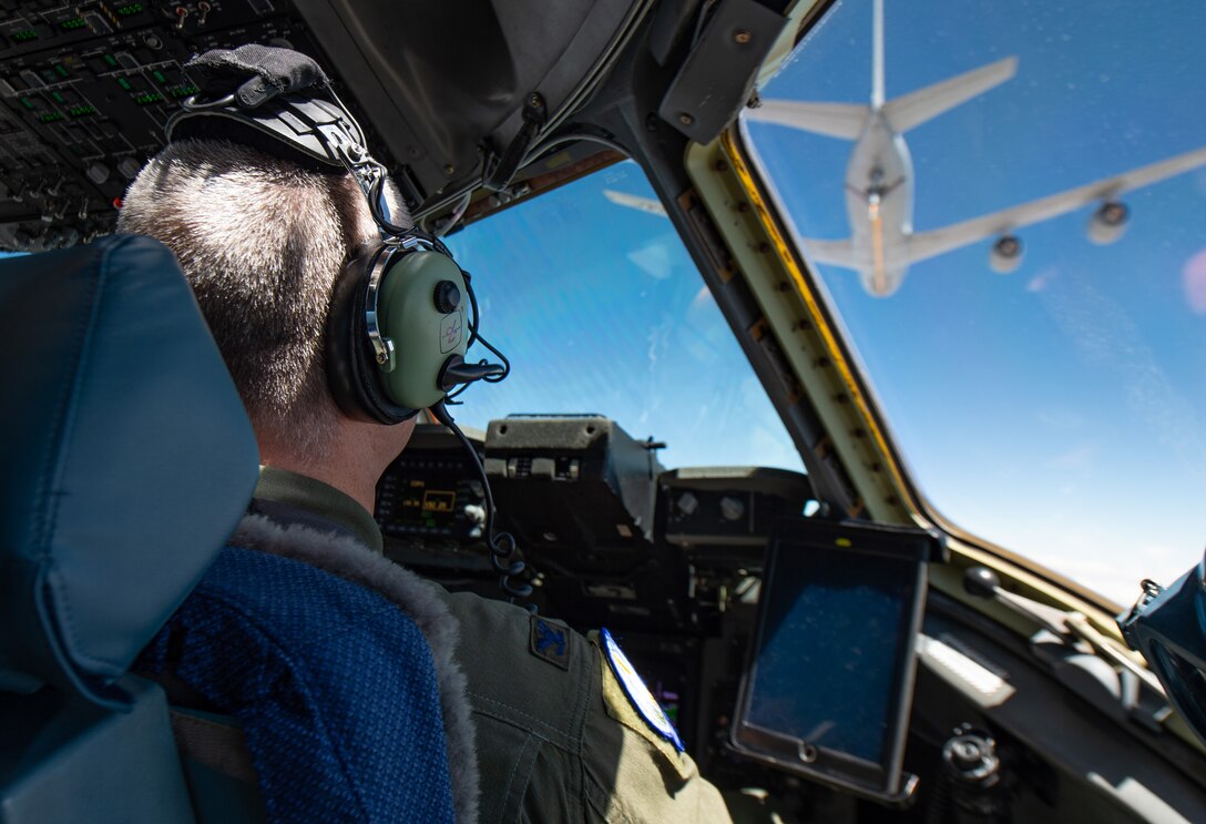 An airman pilots an aircraft while another craft is seen overhead.