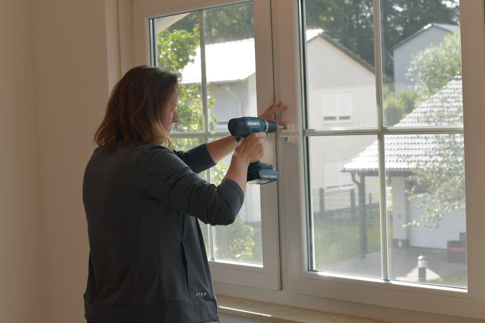 A person screwing on a window handle with a power drill.