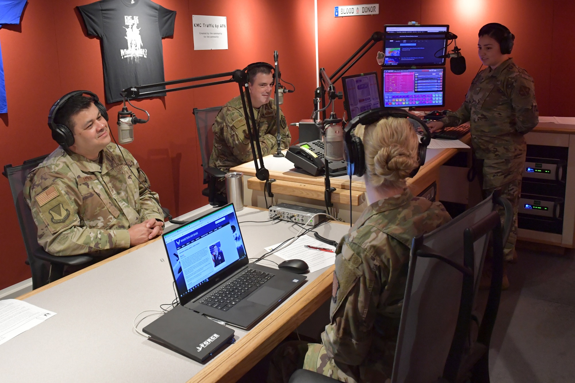 A group of Airmen sitting and standing in a radio station studio.