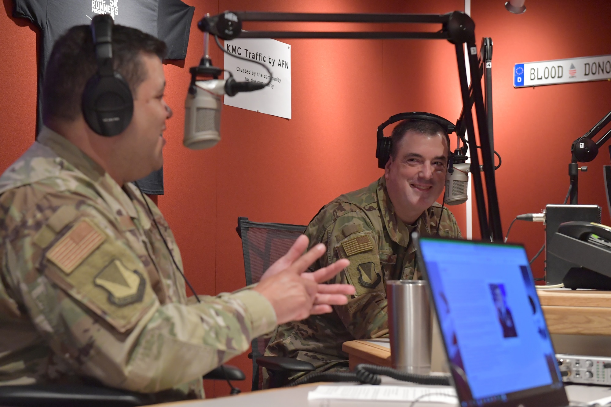 Two Airmen wearing headphones and speaking into microphones at a radio station studio.