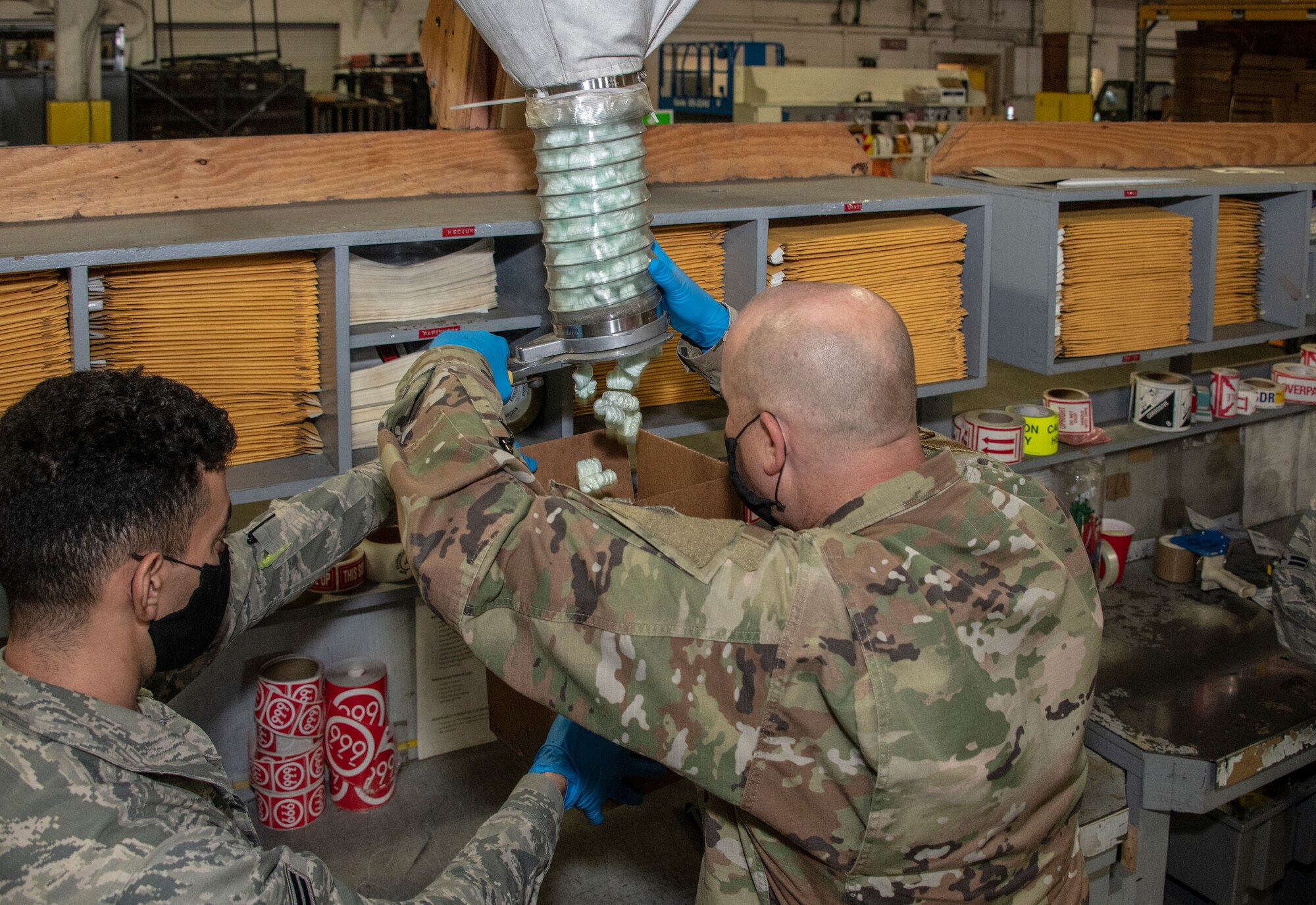 U.S. Air Force Airman 1st Class Yaser Belal, left, 60th Aerial Port Squadron packing and crating technician, assists Chief Master Sgt. Robert Schultz, 60th Air Mobility Wing command chief, add packing peanuts to a box during Leadership Rounds July 24, 2020, at Travis Air Force Base, California. The 60th APS is the United States Transportation Command's primary west coast aerial port providing global and passenger distribution for the United States and its Allies. The Leadership Rounds program provides 60th AMW leadership an opportunity to interact with Airmen and get a detailed view of each mission performed at Travis AFB. (U.S. Air Force photo by Heide Couch)