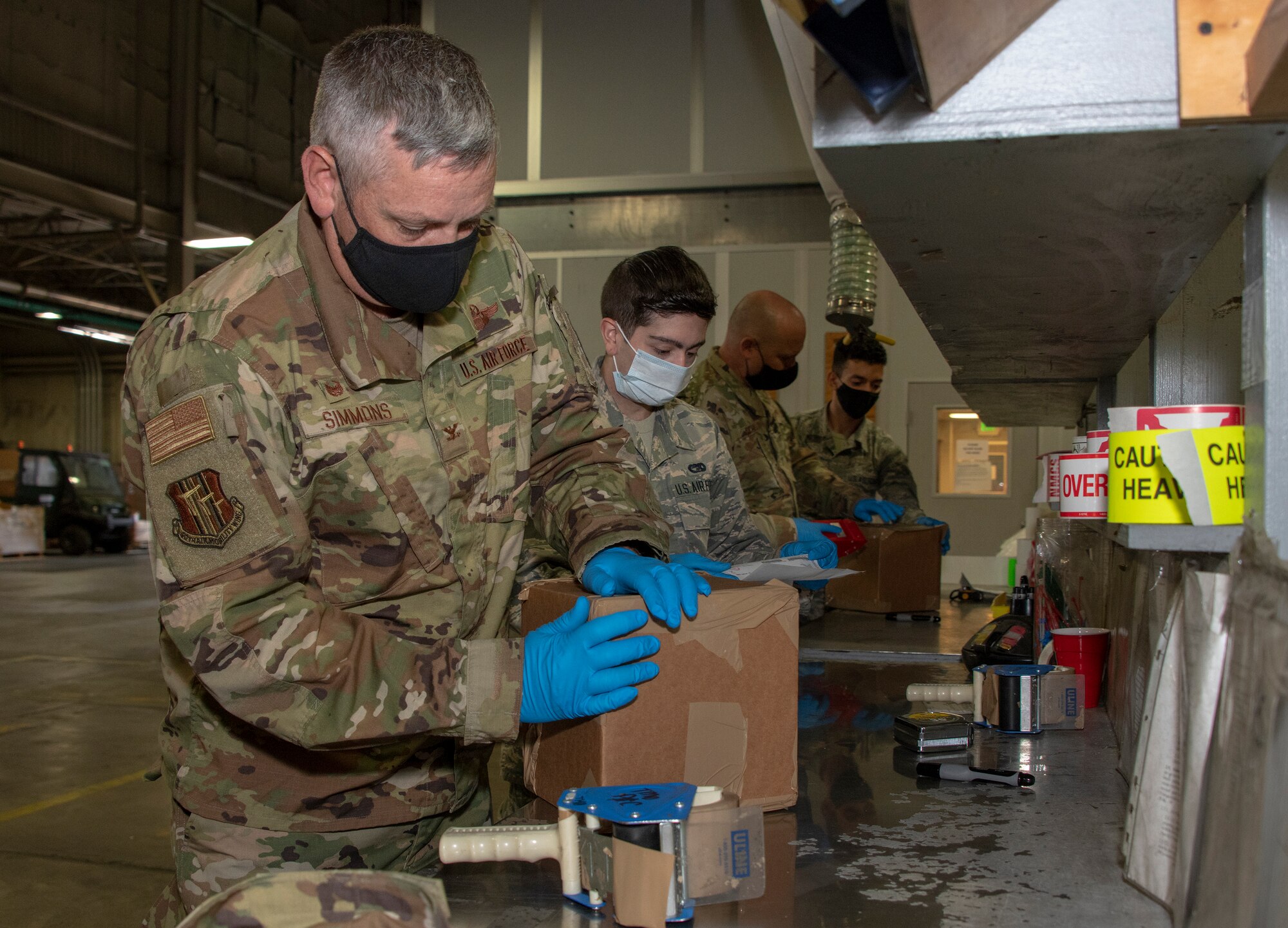 From left, U.S. Air Force Col. Corey Simmons, 60th Air Mobility Wing commander, Airman 1st Class Gregory Concilla, 60th Aerial Port Squadron packing and crating technician, Chief Master Sgt. Robert Schultz, 60th AMW command chief, and A1C Yaser Belal, 60th APS packing and crating technician, participate in a packing and crating demonstration during Leadership Rounds July 24, 2020, at Travis Air Force Base, California. The 60th APS is the United States Transportation Command's primary west coast aerial port providing global and passenger distribution for the United States and its Allies. The Leadership Rounds program provides 60th AMW leadership an opportunity to interact with Airmen and get a detailed view of each mission performed at Travis AFB. (U.S. Air Force photo by Heide Couch)