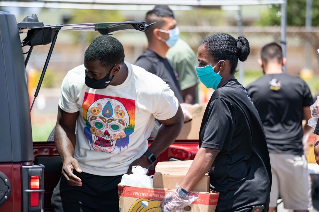 Two soldiers wearing face masks load a box of food into a vehicle.