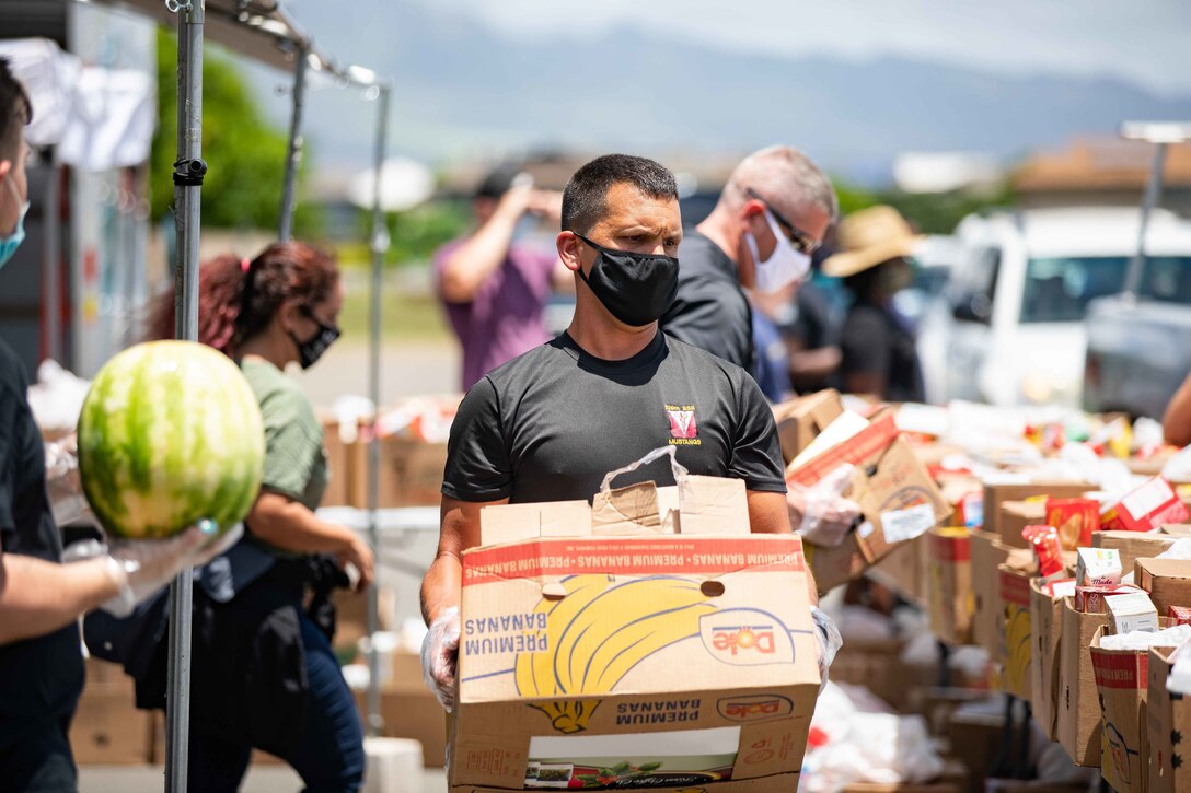 A soldier wearing a face mask carries a box of food.