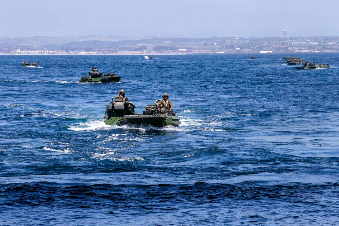 Marines ride in assault amphibious vehicles through waters.