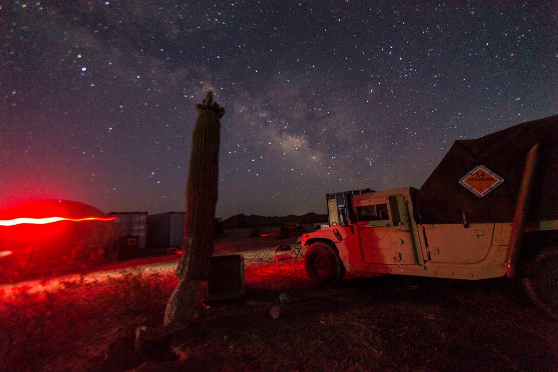 A military vehicle sits parked at night; a red glow shines to the left.