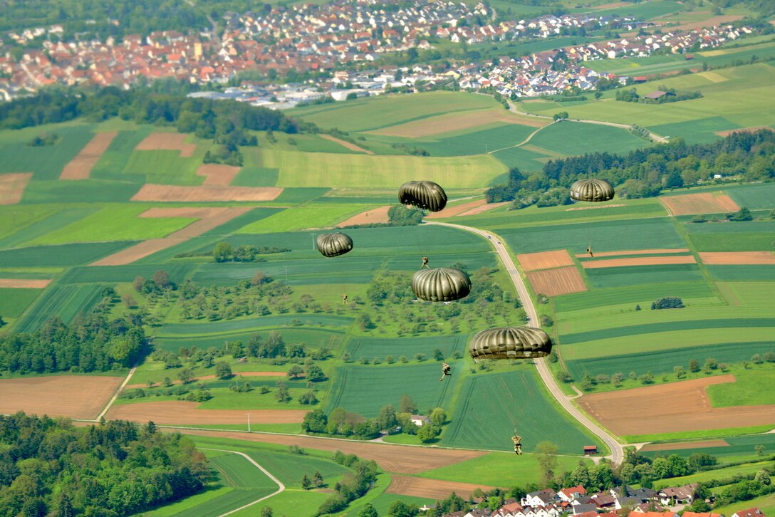 Service members parachute over lush green fields.