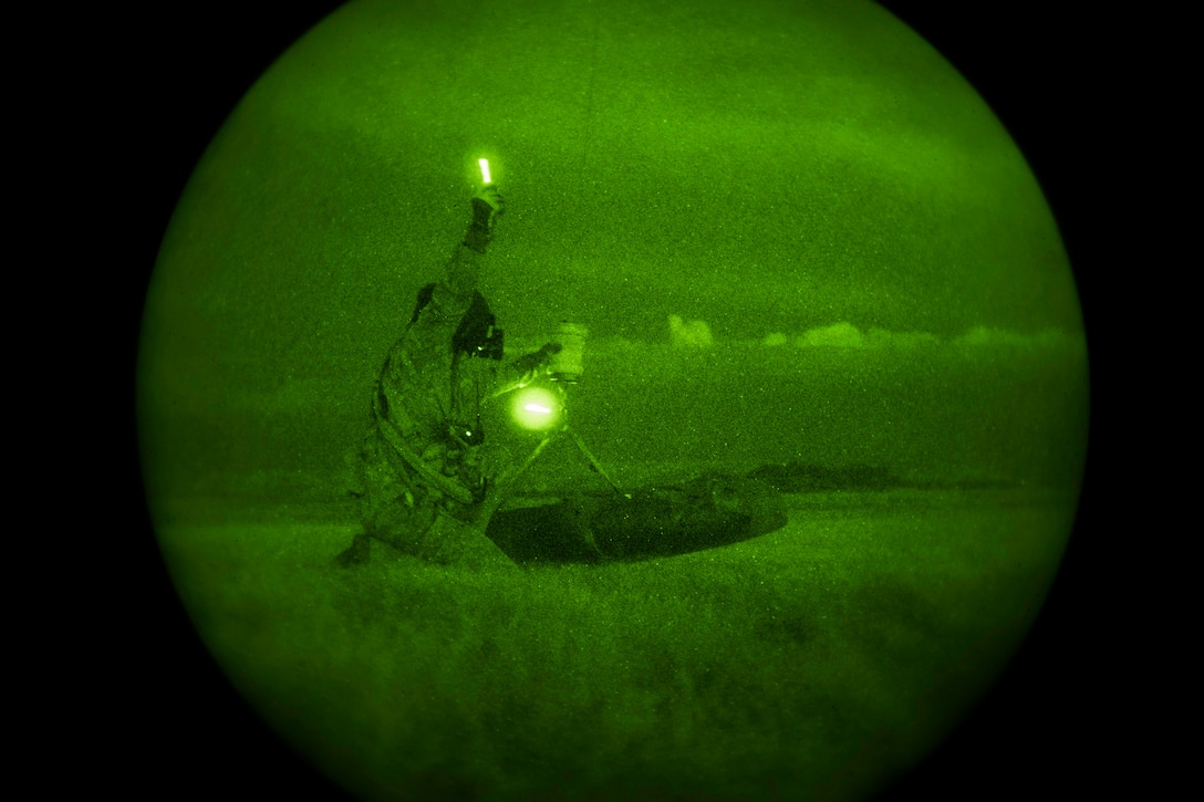 A service member sits in a field-like area illuminated by a green light.