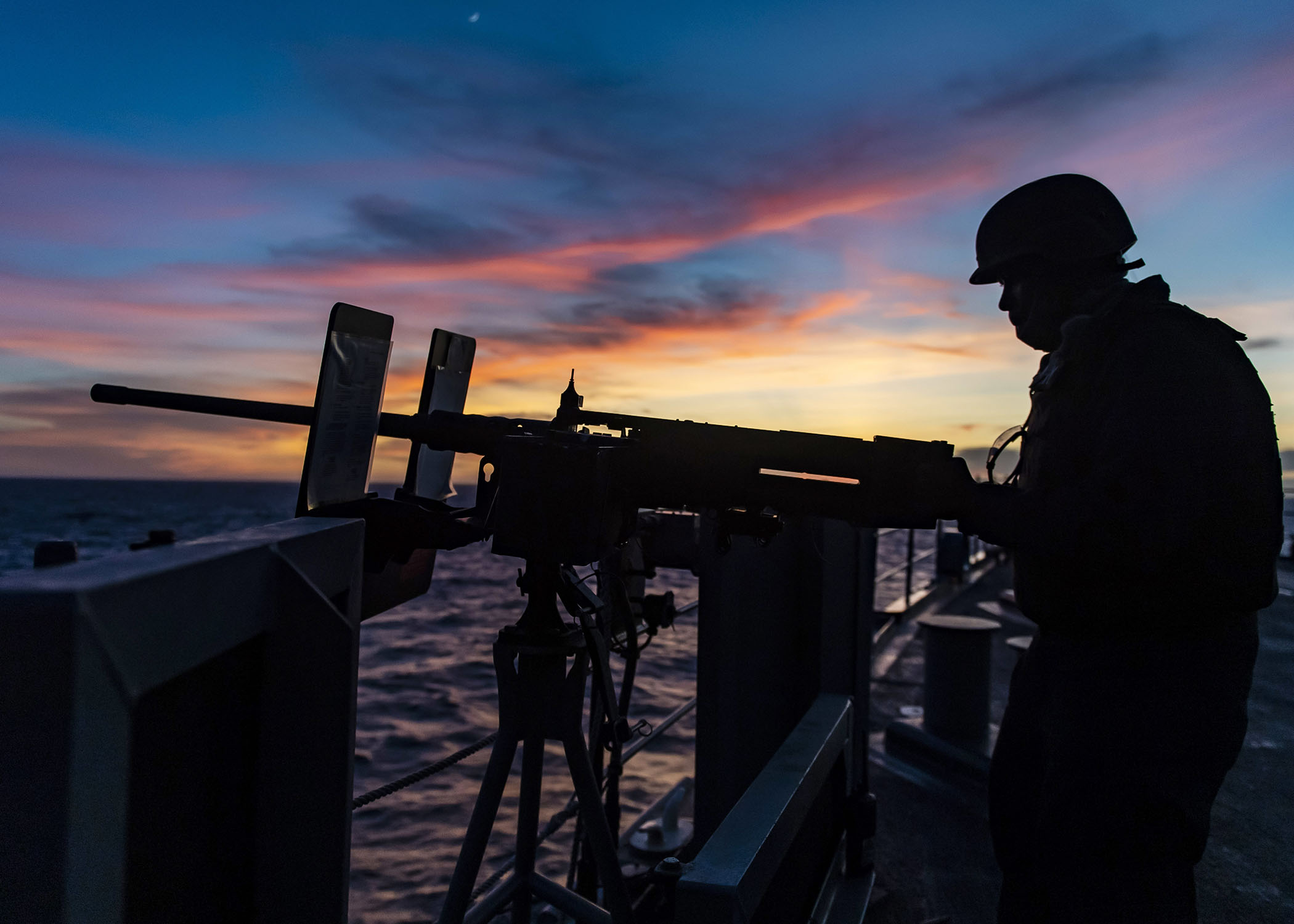 sailor manning a gun at sea during training with sunset in the background