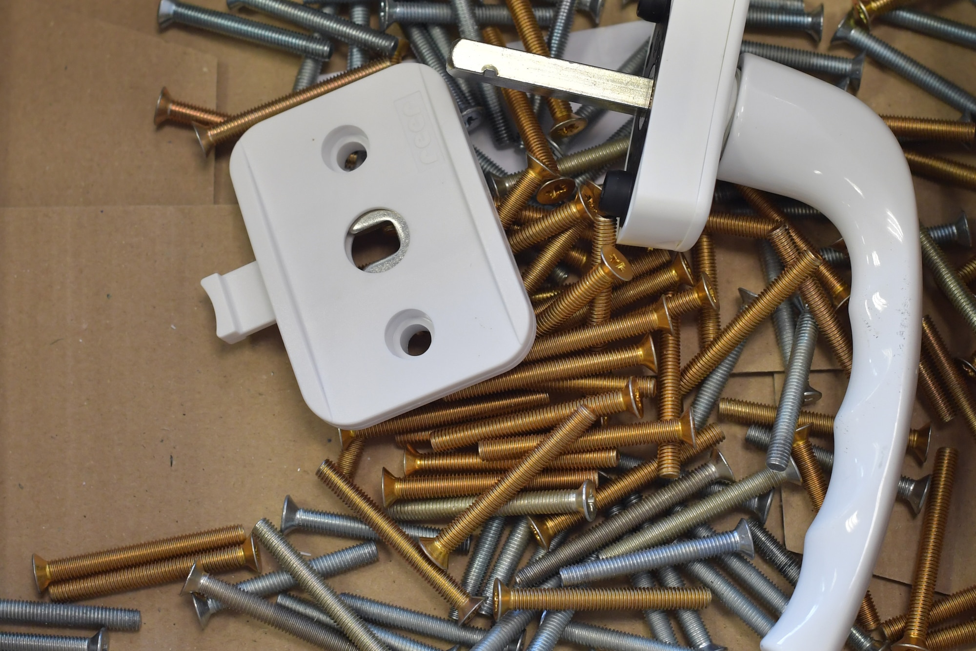 A window handle and lock component laying on a bed of screws.