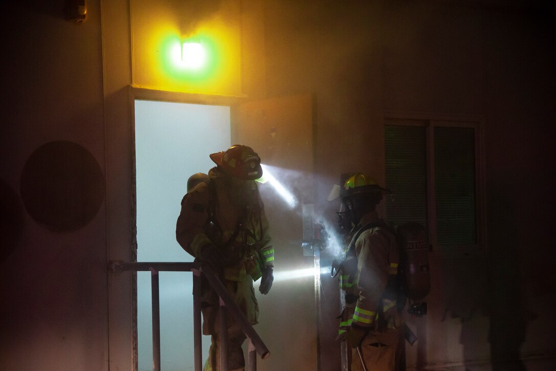 Two Expeditionary Civil Engineer Squadron firefighters exit a smoke-filled building after a fire safety exercise response at Al Udeid Air Base, Qatar, July 24, 2020. Al Udeid AB conducts routine exercises that evaluate and prepare service members to keep them lethal and ready.