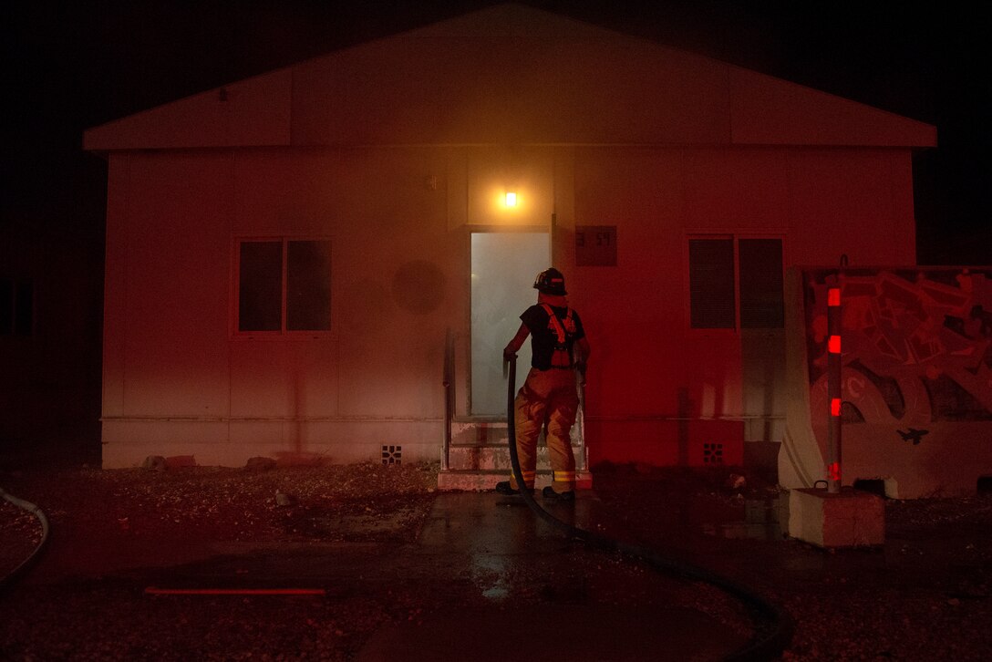 A 379th Expeditionary Civil Engineer Squadron Fire and Emergency Services Flight Airman holds a firehose steady for his teammates inside of a simulated fire safety event during an exercise at Al Udeid Air Base, Qatar, July 24, 2020. The exercise included a fire safety event where Fire and Emergency Services responded to a simulated fire in a building with two unidentified manikins to rescue and provide simulated, on-scene emergency medical care.