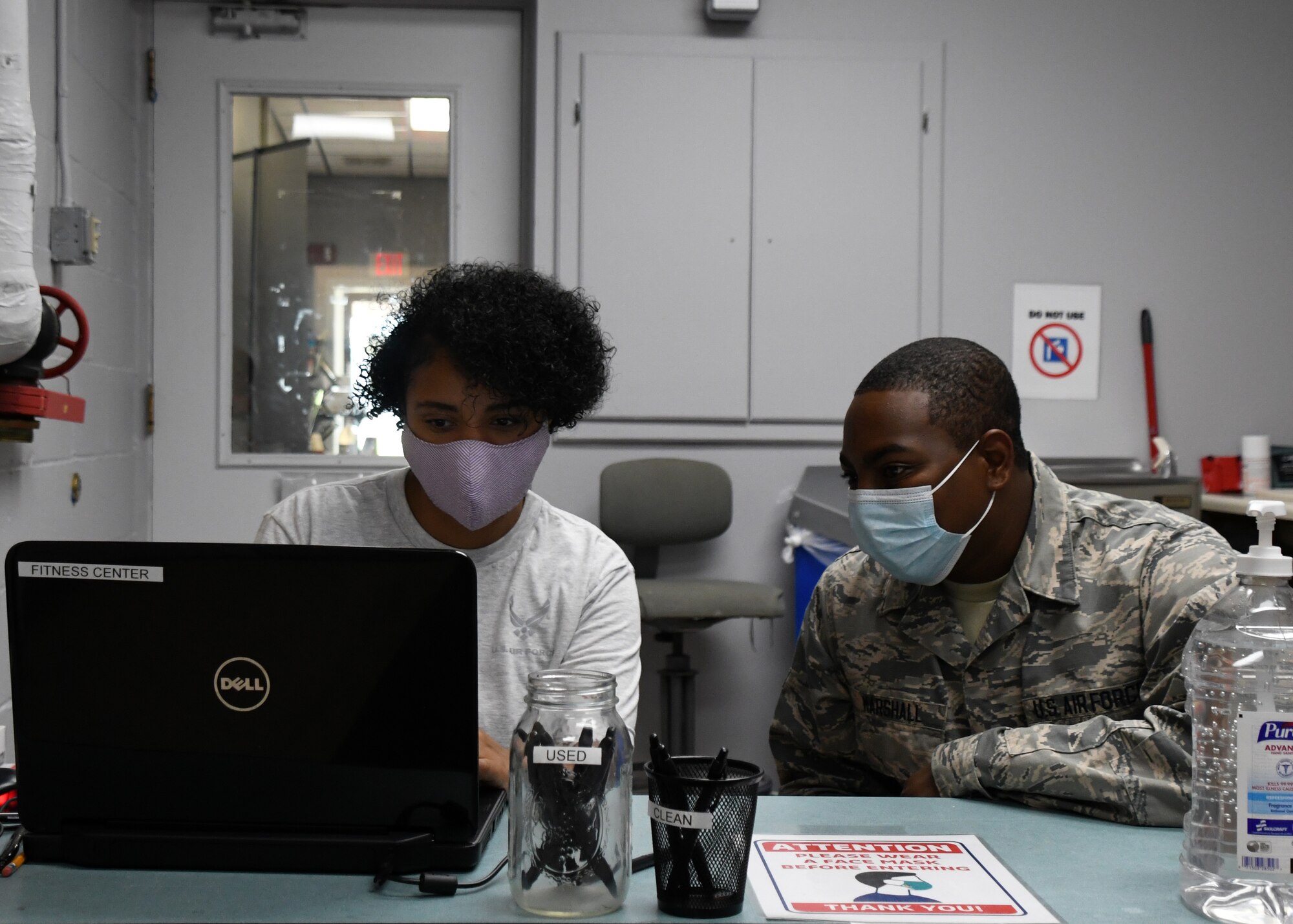 Airman Kyanda Wilson and Airman 1st Class Jason Marshall, Force Support Squadron Airmen, sit at the Base Fitness Room entrance prepared to sign Airmen in to workout, July 24, 2020, at Barnes Air National Guard Base, Massachusetts. Due to the COVID-19 pandemic, wing members who choose to work out need to sign in and follow stricter guidelines in order to maintain a safe and healthy environment.  (U.S. Air National Guard photo by Senior Airman Sara Kolinski)