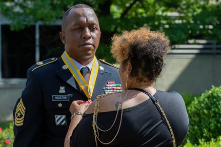 Shani Adams-Houston places a medallion around the neck of her husband, recently retired Sgt. Maj. Ronald Houston, U.S. Army Financial Management Command Operations senior enlisted advisor, shortly after he was presented with the award for being inducted as a distinguished member of the Army Finance Regiment during his retirement ceremony at the Maj. Gen. Emmett J. Bean Federal Center in Indianapolis July 17, 2020. Sergeant Major Houston was born and raised in New Orleans, Louisiana, and he joined the Army as a financial management specialist in May 1992, four days after graduating from high school. (U.S. Army photo by Mark R. W. Orders-Woempner)