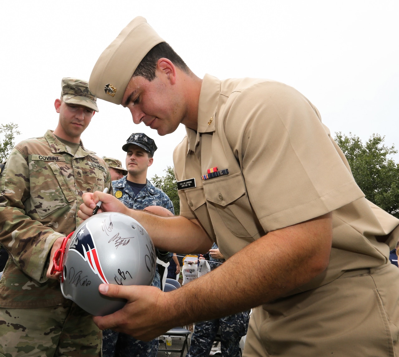 A Navy officer in uniform signs a football helmet.