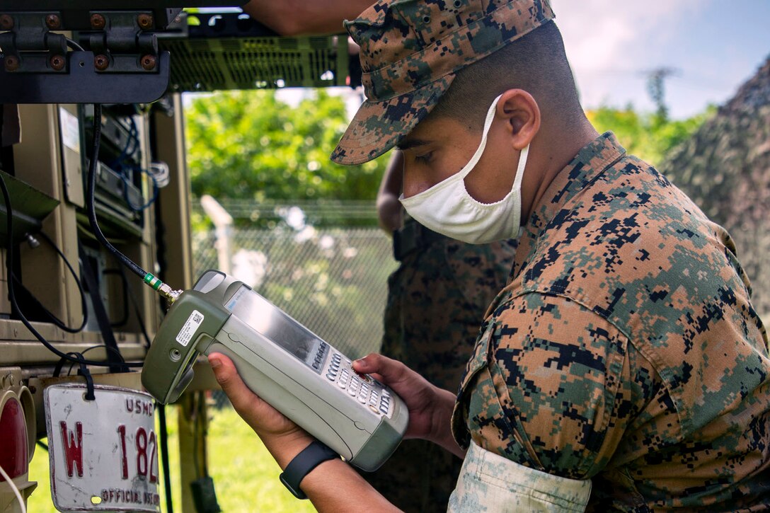 A Marine wearing a face mask holds a piece of communications equipment.