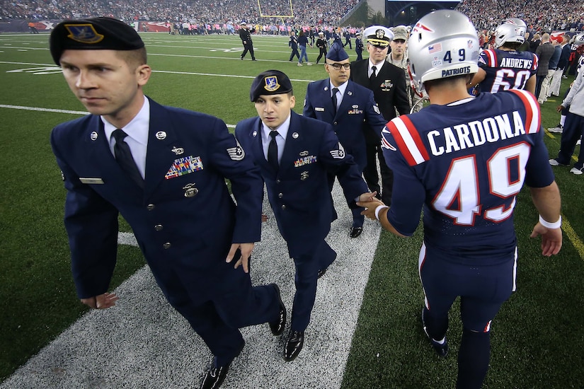 A football player greets fans in uniform along the sidelines of a football field.