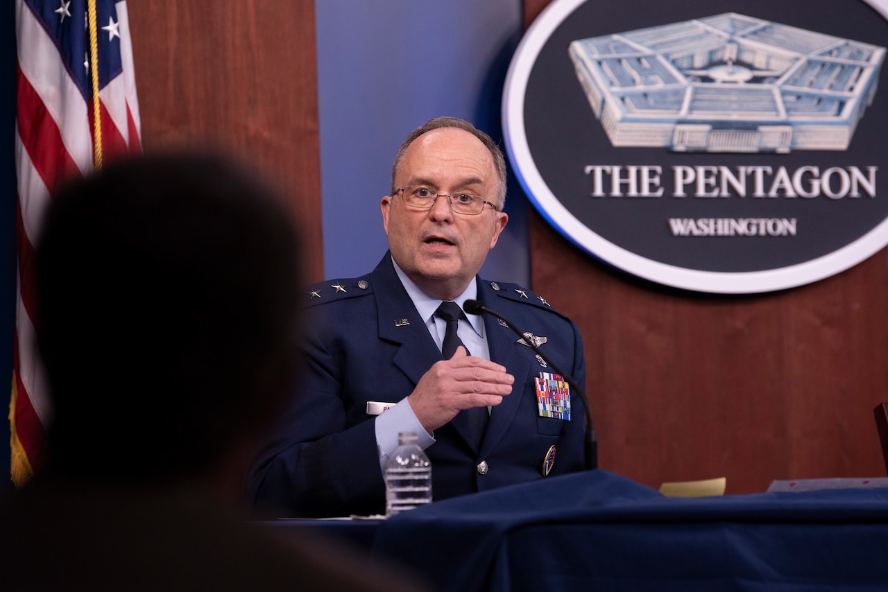 A man in military uniform sits at a table behind a microphone.  Behind him is a sign that reads “The Pentagon - Washington.”