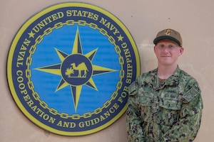 200625-N-IO414-1037 NAVAL SUPPORT ACTIVITY BAHRAIN (June 25, 2020) Ensign Michael Petty poses for a photo in front of U.S. Naval Forces Central Command’s Naval Cooperation and Guidance for Shipping (NCAGS) headquarters. NCAGS serves as a communication link between merchant and military vessels and is made up entirely of U.S. Navy reservists, many of whom are professional merchant marines who leverage their civilian expertise and experience when they report for duty.