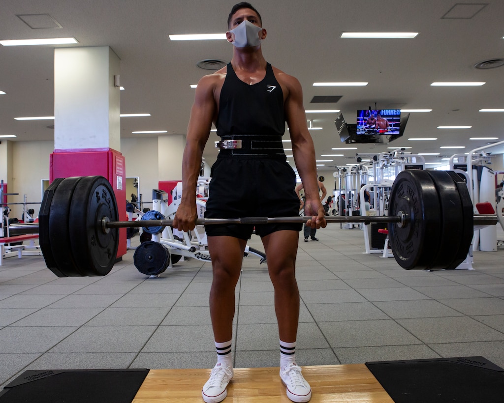 A man wearing a face mask deadlifts a barbell.