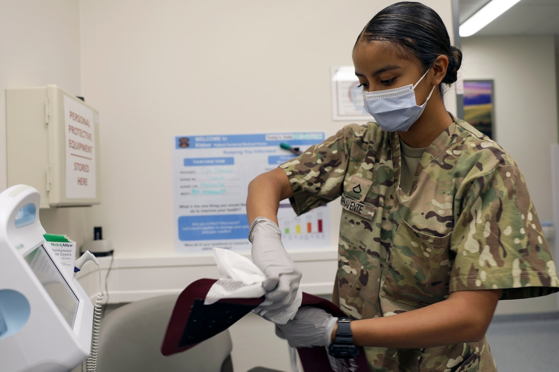 A soldier wearing a face mask wipes down a medical device.