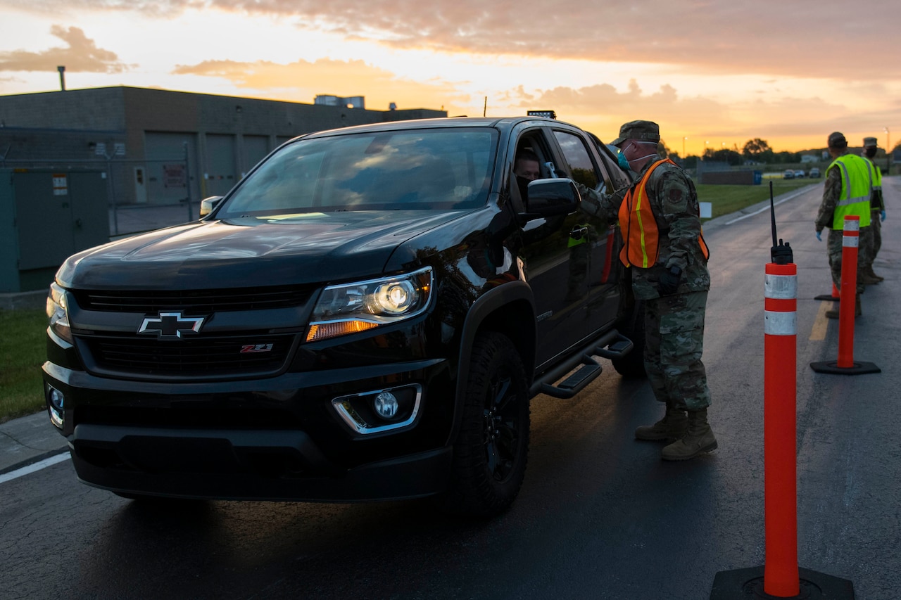 An airman checks the temperature of another airman at a COVID-19 prescreening station.