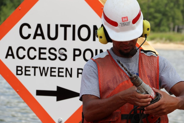 Man in front of sign that reads, "CAUTION Access Point Between Reefs" and holds drill