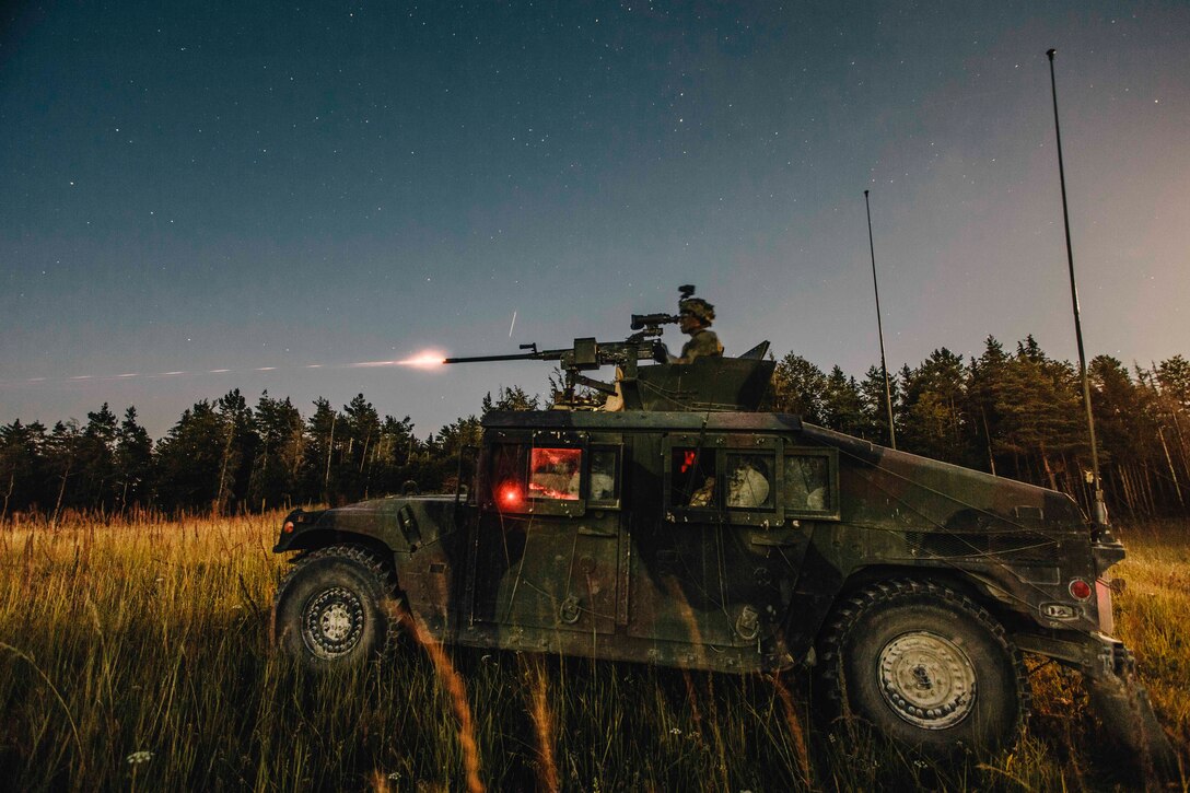 A soldier stands inside a military vehicle firing a weapon.