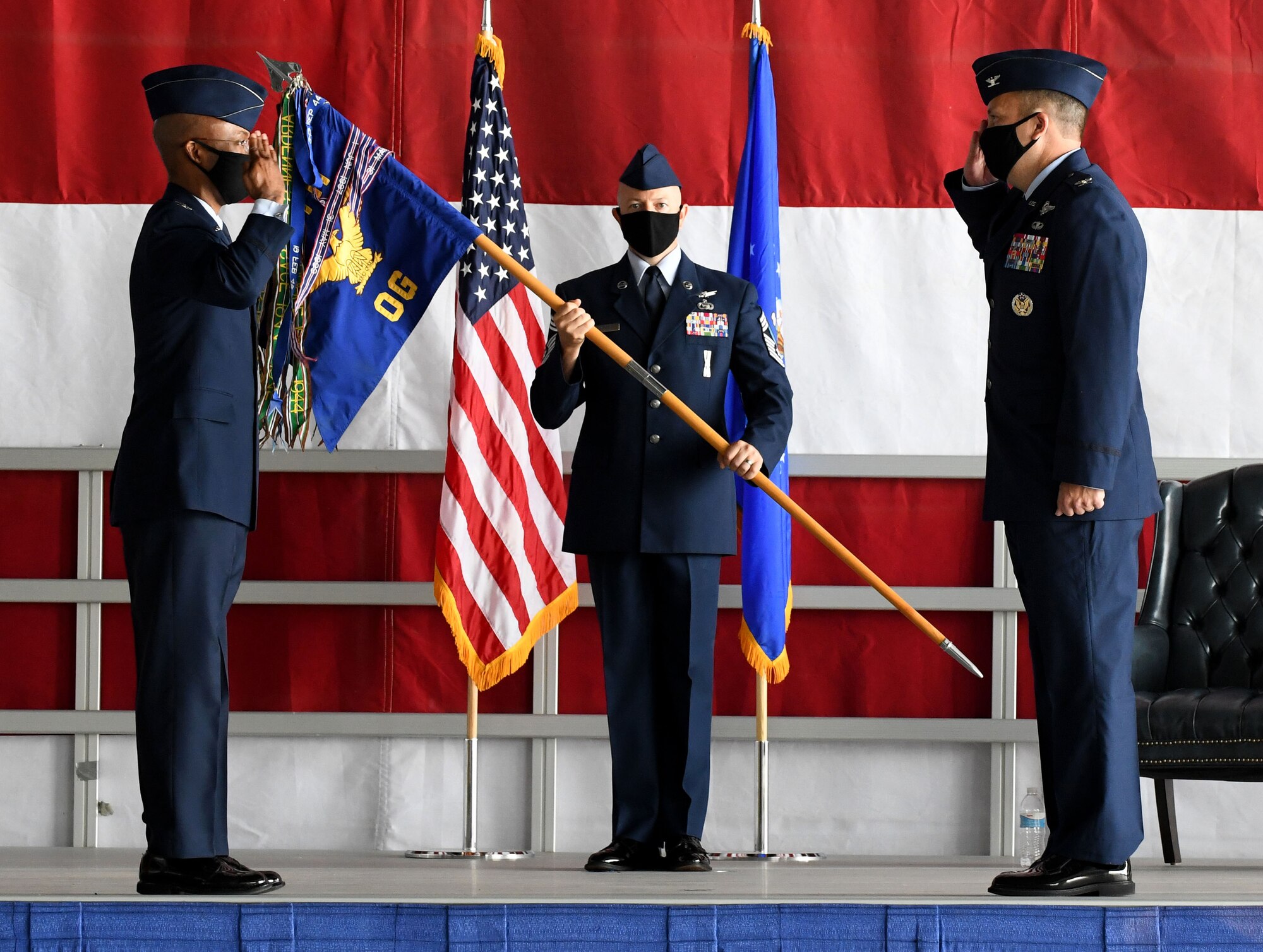 Two Airmen salute each other while a third looks on holding a guideon