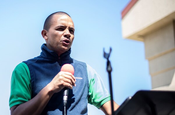 A man with a buzzed head wearing a sweater vest speaks into a microphone